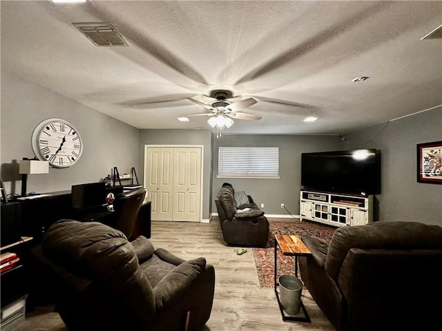 living room with a textured ceiling, ceiling fan, visible vents, baseboards, and light wood-type flooring