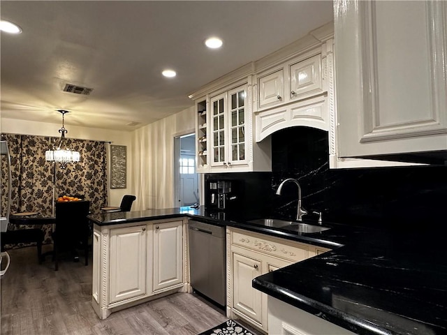 kitchen with a peninsula, stainless steel dishwasher, dark countertops, and a sink