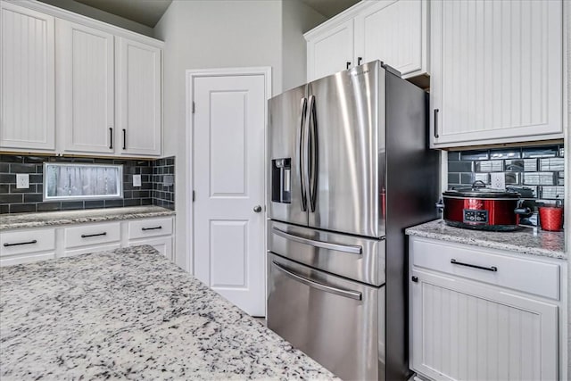 kitchen featuring white cabinets, stainless steel fridge, tasteful backsplash, and light stone countertops