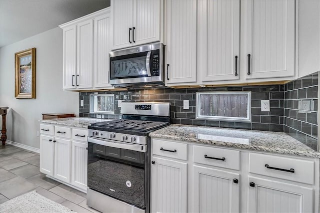 kitchen with white cabinetry, light stone countertops, decorative backsplash, light tile patterned flooring, and appliances with stainless steel finishes