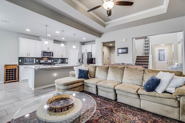 living room with a raised ceiling, ceiling fan, ornamental molding, and sink