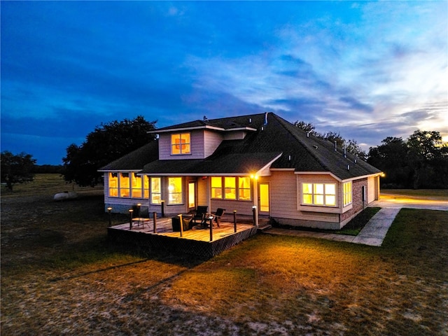 back house at dusk featuring a yard, a sunroom, and a wooden deck