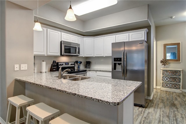 kitchen with kitchen peninsula, decorative light fixtures, a kitchen bar, white cabinetry, and stainless steel appliances