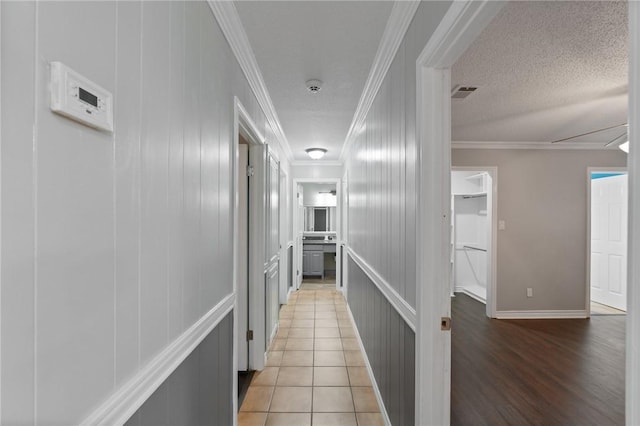 corridor with visible vents, ornamental molding, a textured ceiling, light tile patterned floors, and attic access