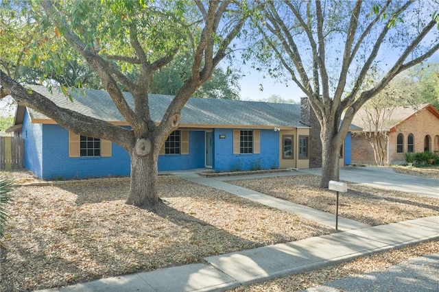 ranch-style home with fence, brick siding, driveway, and roof with shingles