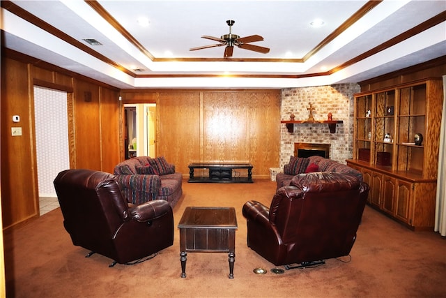 carpeted living room featuring a fireplace, a tray ceiling, ceiling fan, and wooden walls