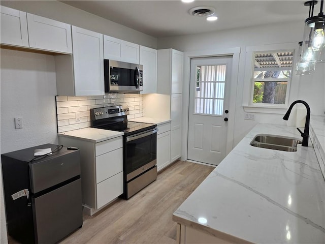 kitchen with sink, white cabinetry, hanging light fixtures, stainless steel appliances, and light stone countertops