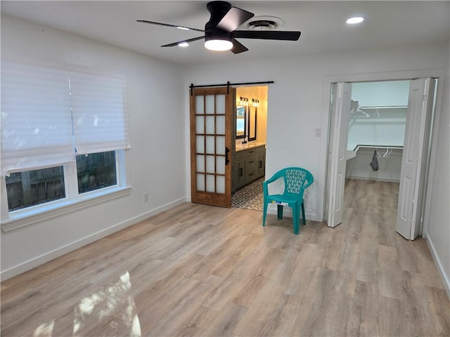 unfurnished room featuring ceiling fan, a barn door, and light wood-type flooring