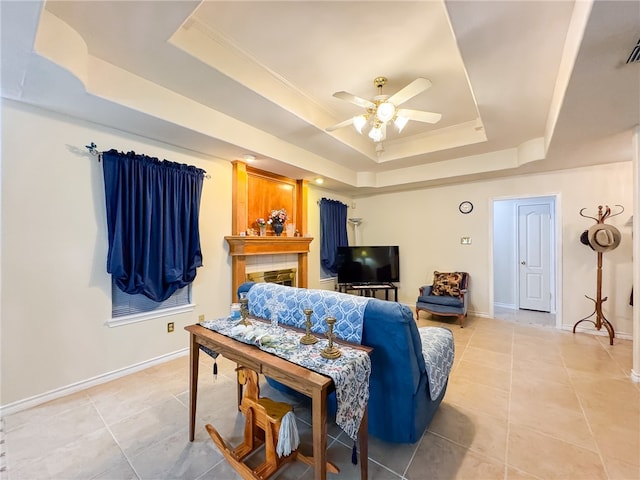 tiled living room with ornamental molding, a tray ceiling, ceiling fan, and a fireplace