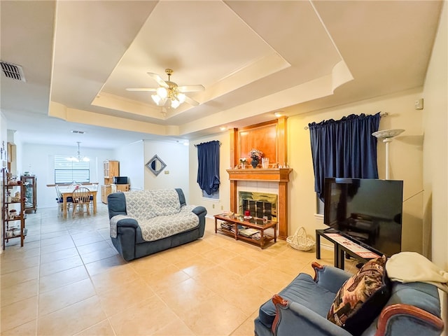 tiled living room featuring ceiling fan with notable chandelier, a tile fireplace, and a tray ceiling