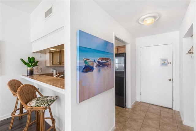 kitchen with tile countertops, light tile patterned floors, a kitchen breakfast bar, stainless steel fridge, and kitchen peninsula