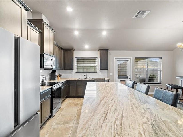 7717 Pruet Dr, Corpus Christi, TX 78414 - kitchen with appliances with stainless steel finishes, light stone countertops, light tile patterned floors, dark brown cabinetry, and recessed lighting