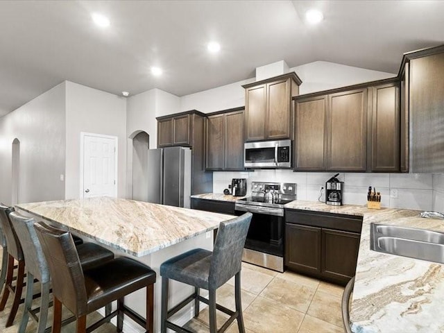 7717 Pruet Dr, Corpus Christi, TX 78414 - kitchen with appliances with stainless steel finishes, arched walkways, a kitchen breakfast bar, dark brown cabinets, and backsplash