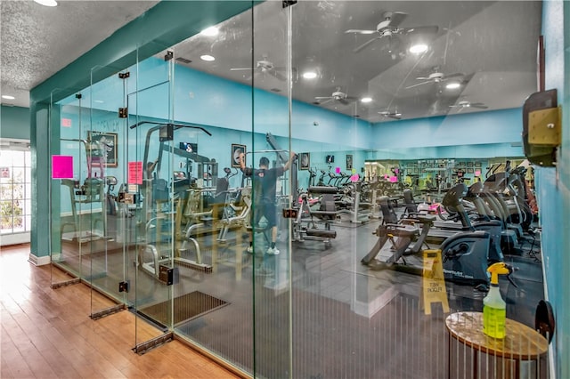 exercise room with ceiling fan, wood-type flooring, and a textured ceiling