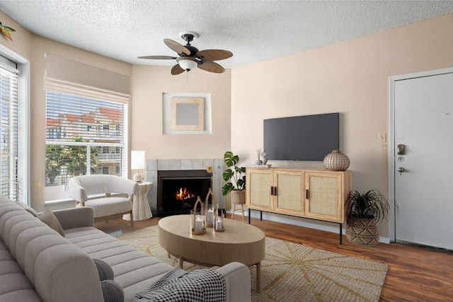 living room featuring dark hardwood / wood-style flooring, ceiling fan, a tiled fireplace, and a textured ceiling