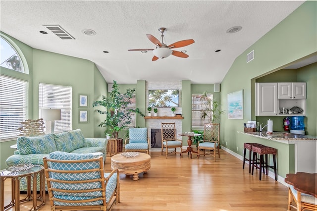 living room featuring ceiling fan, lofted ceiling, a textured ceiling, and light hardwood / wood-style floors