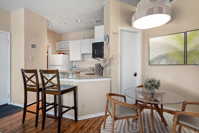 kitchen with white cabinetry, dark hardwood / wood-style flooring, white refrigerator, kitchen peninsula, and a textured ceiling