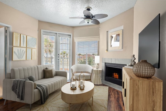 living room with french doors, wood-type flooring, a textured ceiling, ceiling fan, and a tiled fireplace