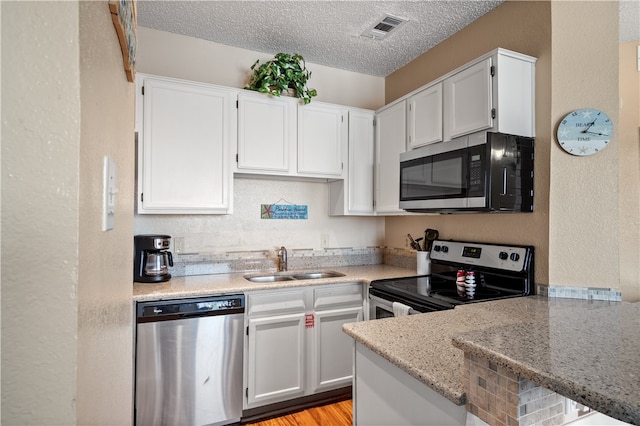 kitchen with appliances with stainless steel finishes, sink, white cabinets, kitchen peninsula, and light stone countertops