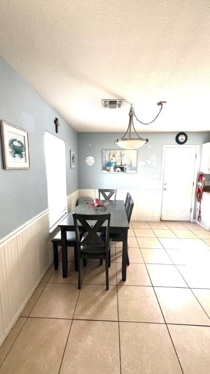 dining area featuring a wainscoted wall, light tile patterned flooring, a textured ceiling, and visible vents