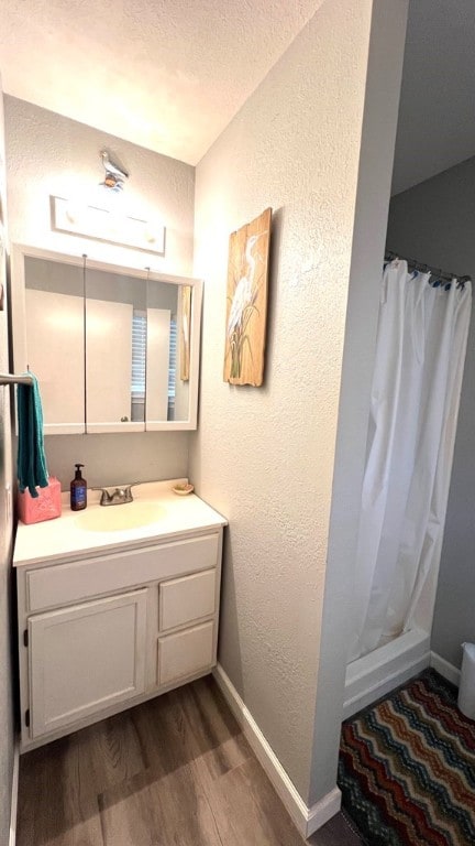 full bathroom with a shower with curtain, wood finished floors, baseboards, vanity, and a textured wall