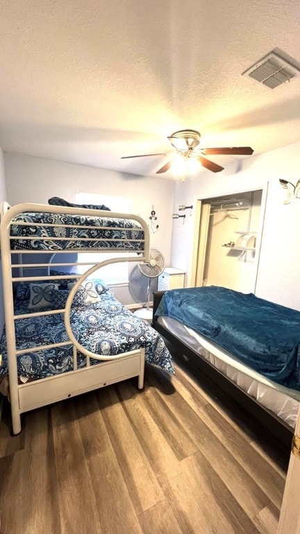 bedroom featuring ceiling fan, a textured ceiling, visible vents, and wood finished floors