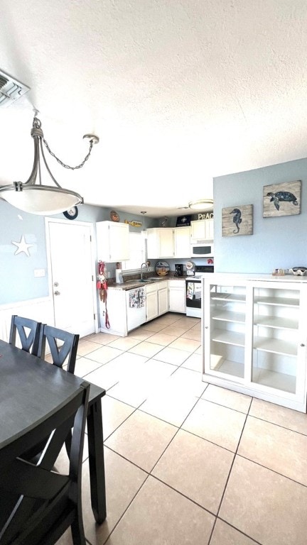 kitchen featuring a textured ceiling, stove, white cabinetry, light tile patterned floors, and white microwave