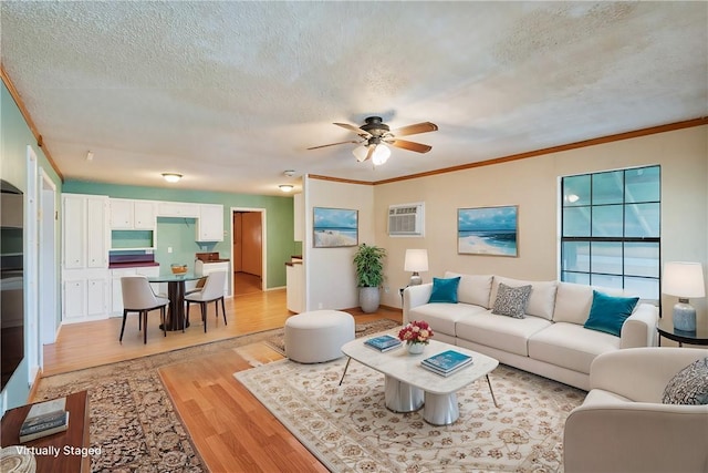 living area featuring a textured ceiling, ceiling fan, light wood-style flooring, an AC wall unit, and crown molding