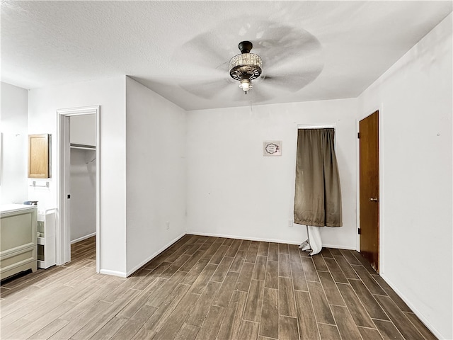 unfurnished bedroom featuring ceiling fan, a spacious closet, hardwood / wood-style floors, a textured ceiling, and a closet