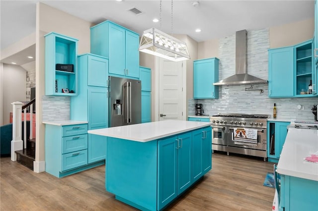 kitchen with a center island, high end appliances, wall chimney exhaust hood, blue cabinetry, and light hardwood / wood-style floors