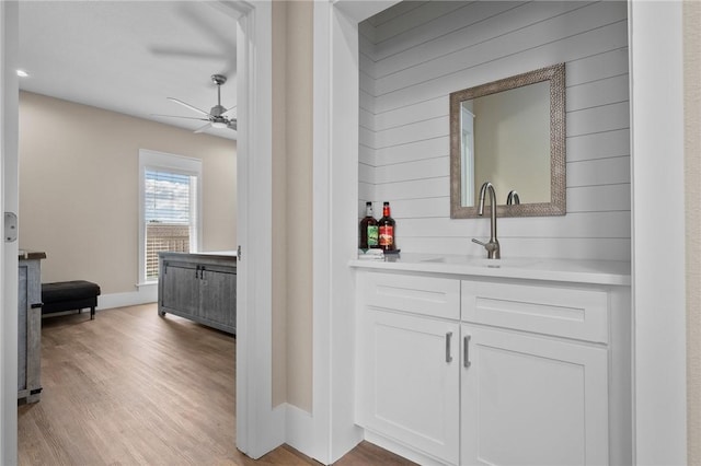 bar with ceiling fan, sink, light hardwood / wood-style floors, wooden walls, and white cabinets