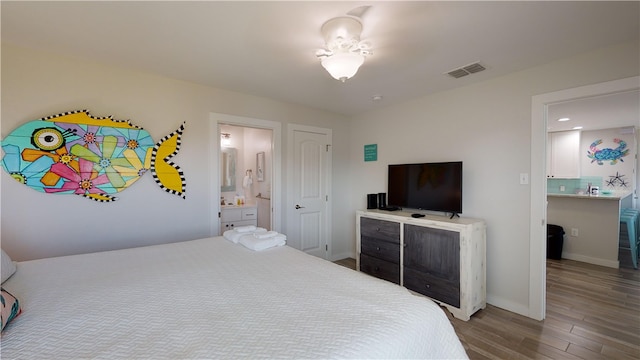 bedroom featuring visible vents, ensuite bathroom, baseboards, and wood finished floors