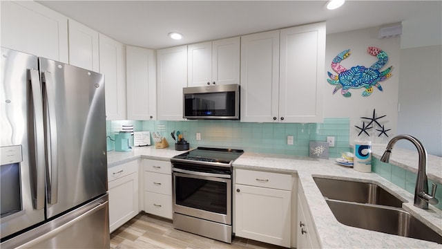 kitchen featuring tasteful backsplash, appliances with stainless steel finishes, light stone counters, white cabinetry, and a sink