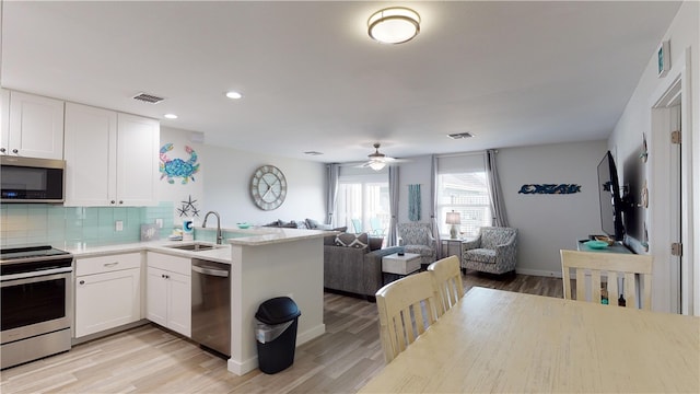 kitchen featuring a sink, white cabinets, open floor plan, light countertops, and appliances with stainless steel finishes