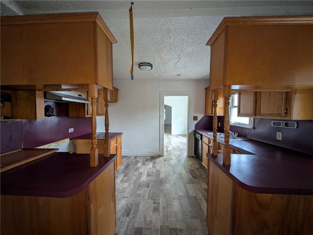 kitchen with brown cabinets, wood finished floors, dark countertops, under cabinet range hood, and a textured ceiling