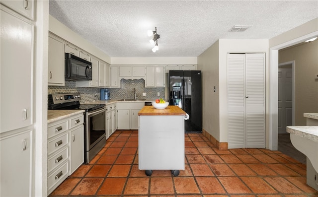 kitchen featuring butcher block counters, sink, black appliances, a center island, and decorative backsplash