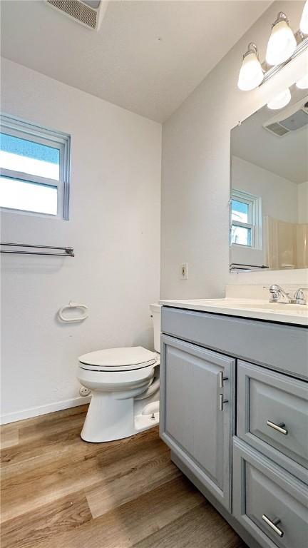 bathroom featuring plenty of natural light, toilet, wood finished floors, and visible vents
