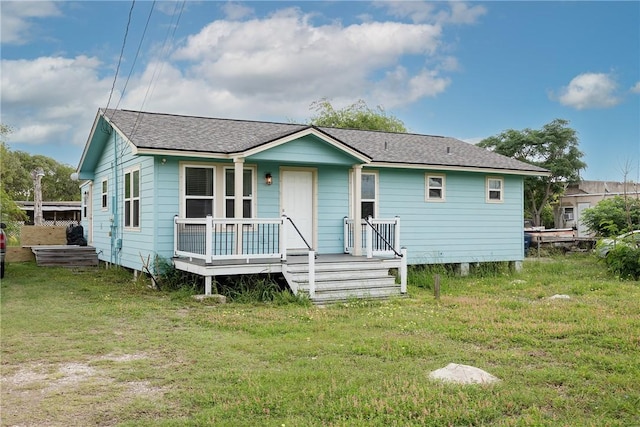 rear view of house with a yard, a shingled roof, and a porch