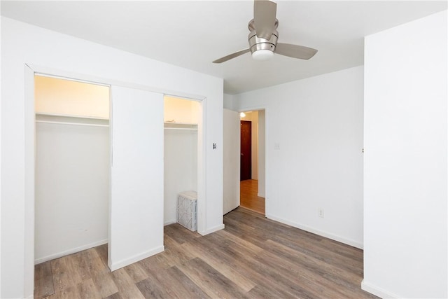 unfurnished bedroom featuring baseboards, ceiling fan, multiple closets, and light wood-style flooring