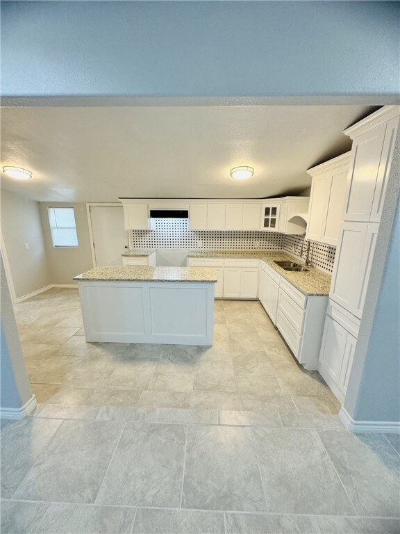 kitchen with white cabinetry, sink, light stone counters, a kitchen island, and decorative backsplash