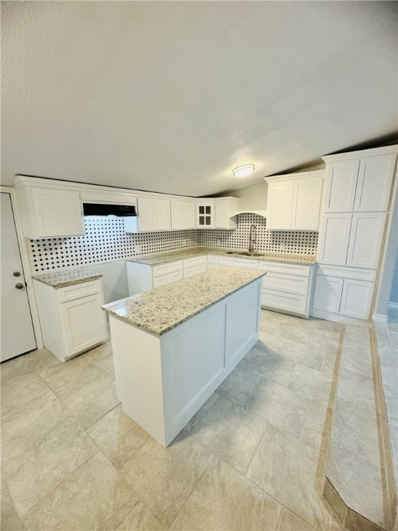 kitchen with white cabinets, light stone countertops, backsplash, and a kitchen island