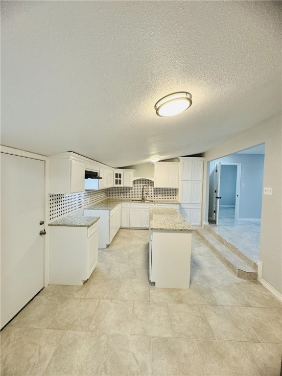 kitchen featuring light stone counters, tasteful backsplash, a textured ceiling, a center island, and white cabinets