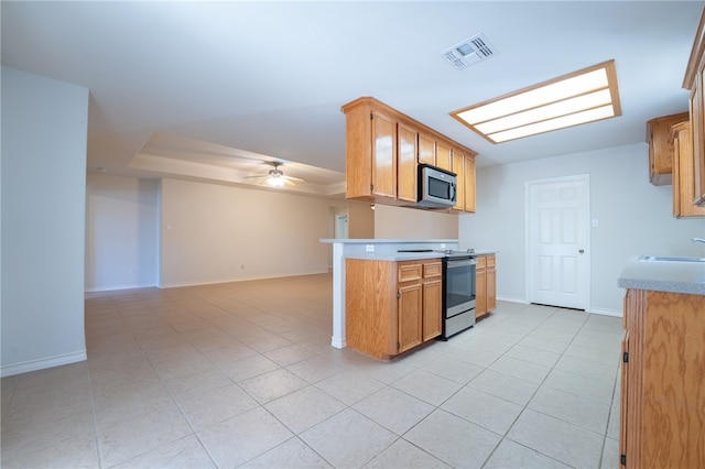 kitchen with sink, ceiling fan, light tile patterned floors, a tray ceiling, and stainless steel appliances