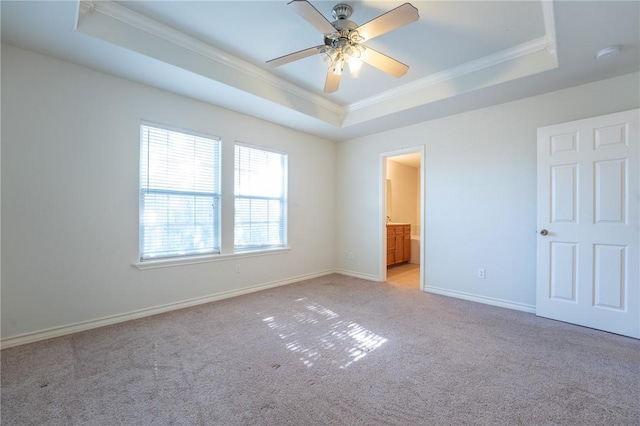 unfurnished bedroom with light carpet, ensuite bathroom, ceiling fan, ornamental molding, and a tray ceiling