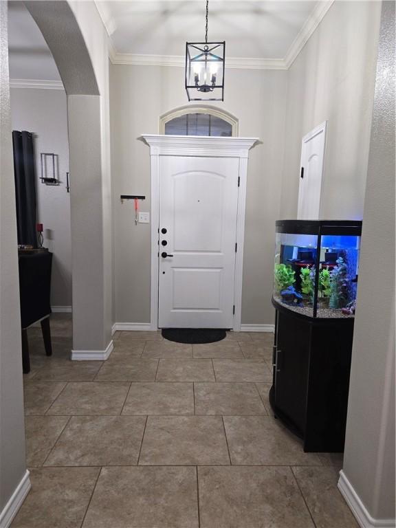 entryway with arched walkways, a chandelier, light tile patterned flooring, baseboards, and crown molding