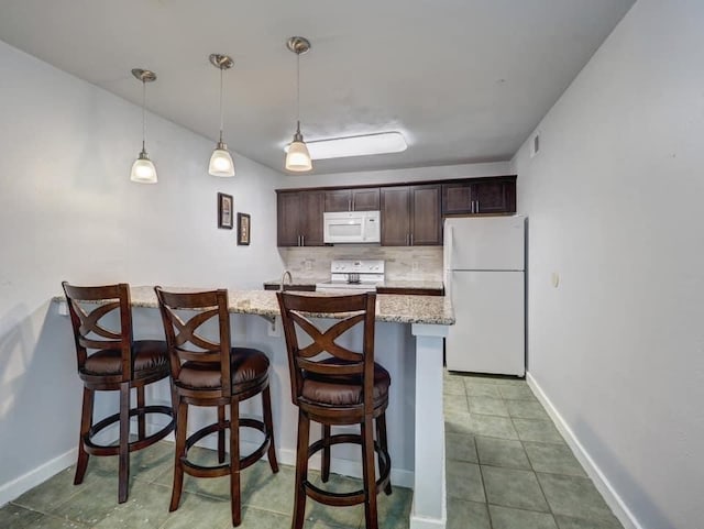 kitchen with a breakfast bar area, white appliances, dark brown cabinets, pendant lighting, and decorative backsplash