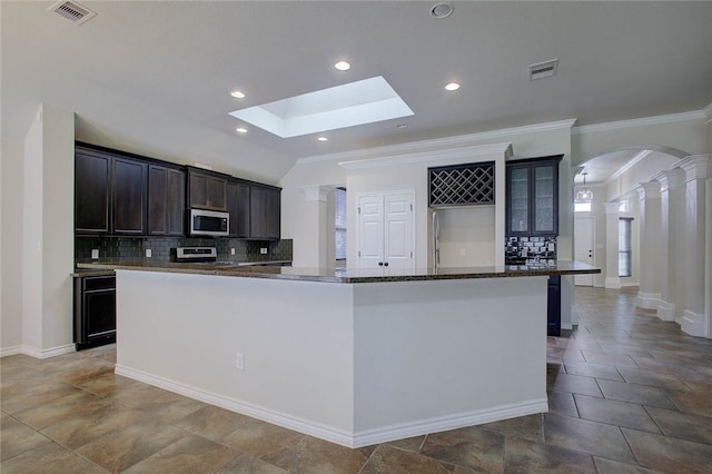 kitchen with ornate columns, a skylight, a center island with sink, dark stone countertops, and stove