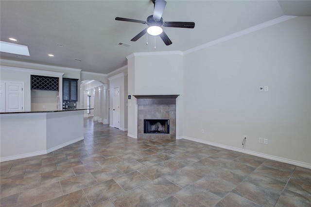 unfurnished living room featuring a tiled fireplace, ornamental molding, and ceiling fan