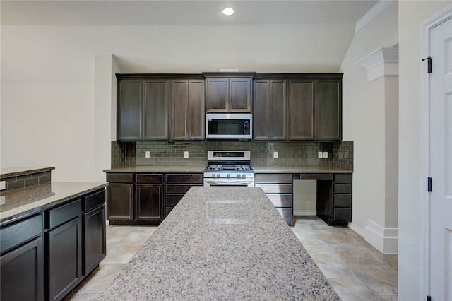 kitchen with stainless steel appliances, light stone countertops, dark brown cabinets, and decorative backsplash