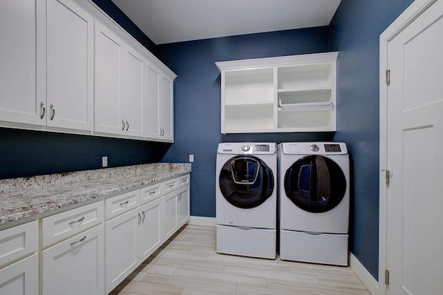 clothes washing area featuring separate washer and dryer, light wood-style floors, cabinet space, and baseboards